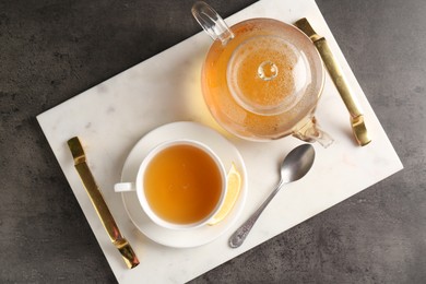 Photo of Refreshing green tea, spoon and slice of lemon served on dark textured table, top view