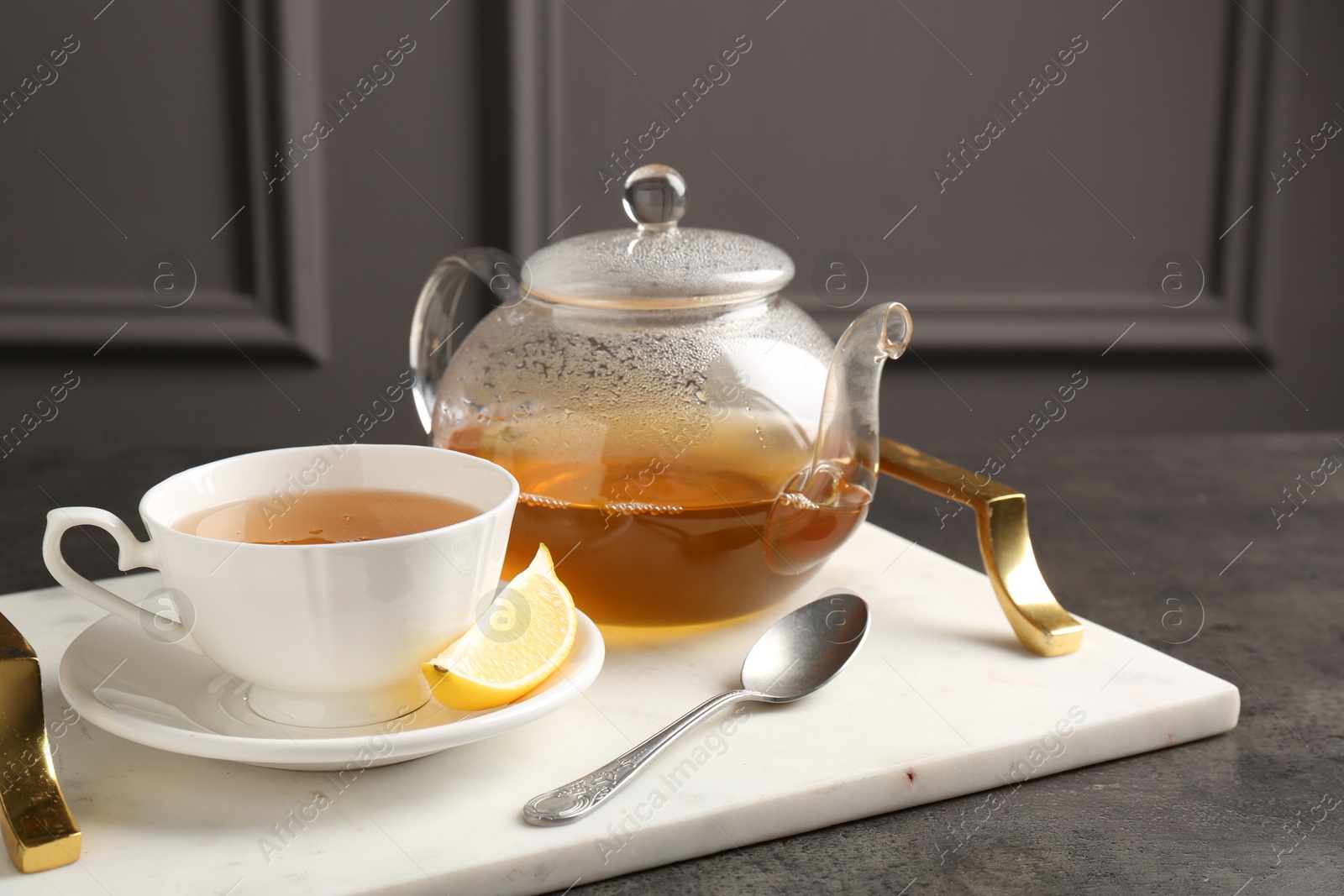 Photo of Refreshing green tea, spoon and slice of lemon served on dark textured table, closeup