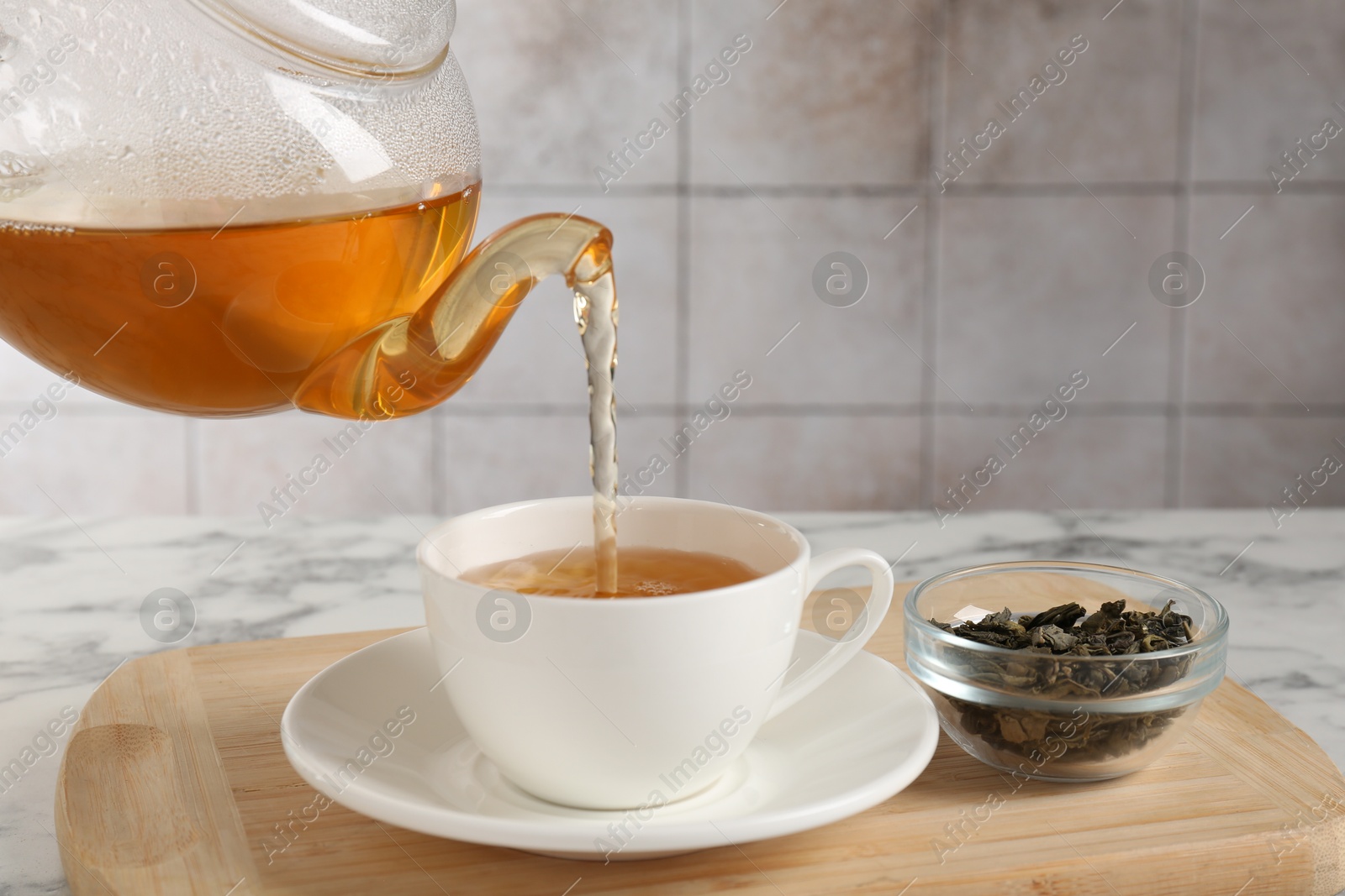 Photo of Pouring refreshing green tea from teapot into cup at white marble table, closeup