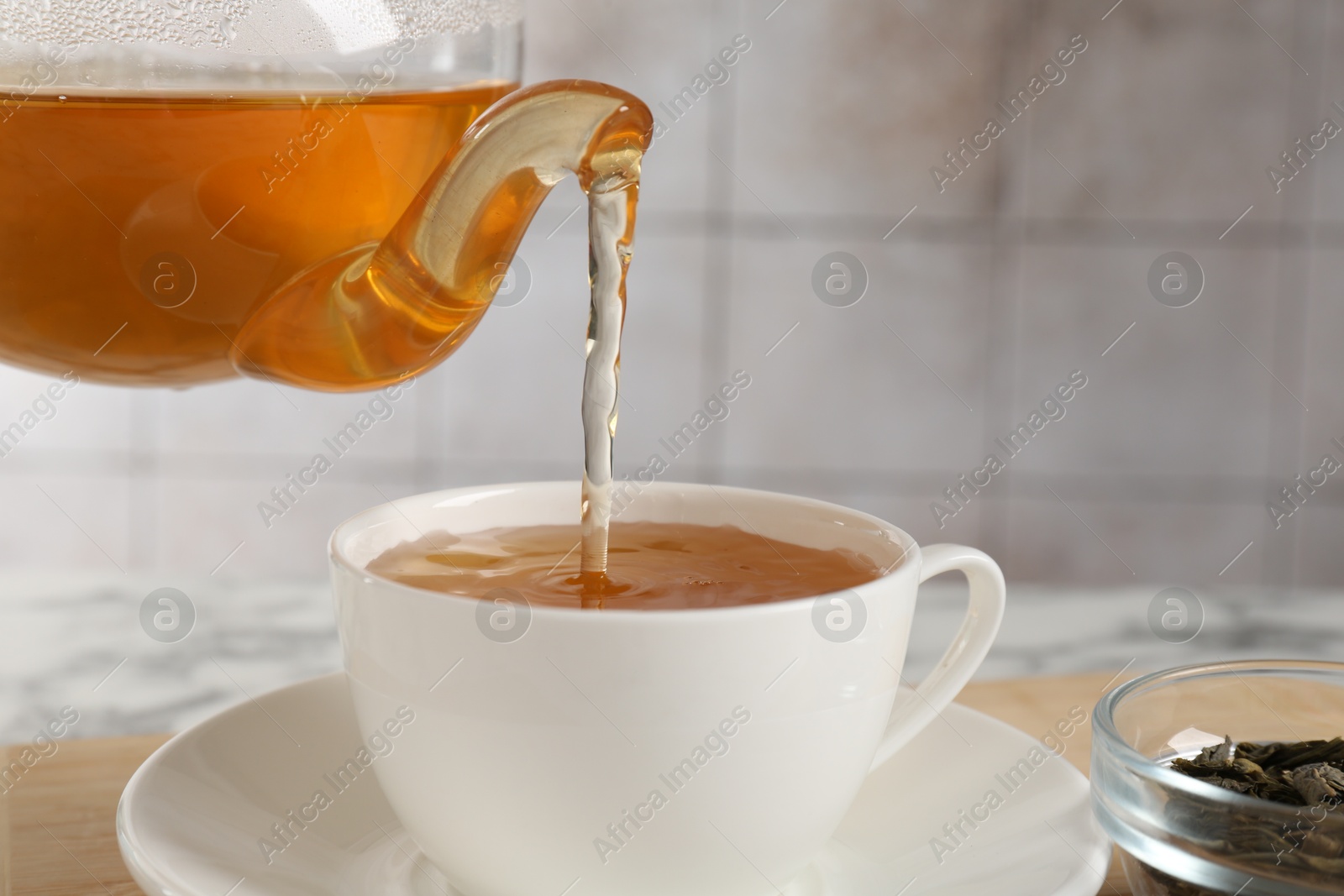 Photo of Pouring refreshing green tea from teapot into cup at table, closeup