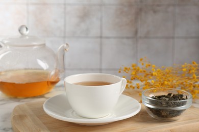 Photo of Refreshing green tea and dry leaves on white marble table, closeup