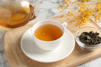 Photo of Refreshing green tea and dry leaves on white marble table, closeup