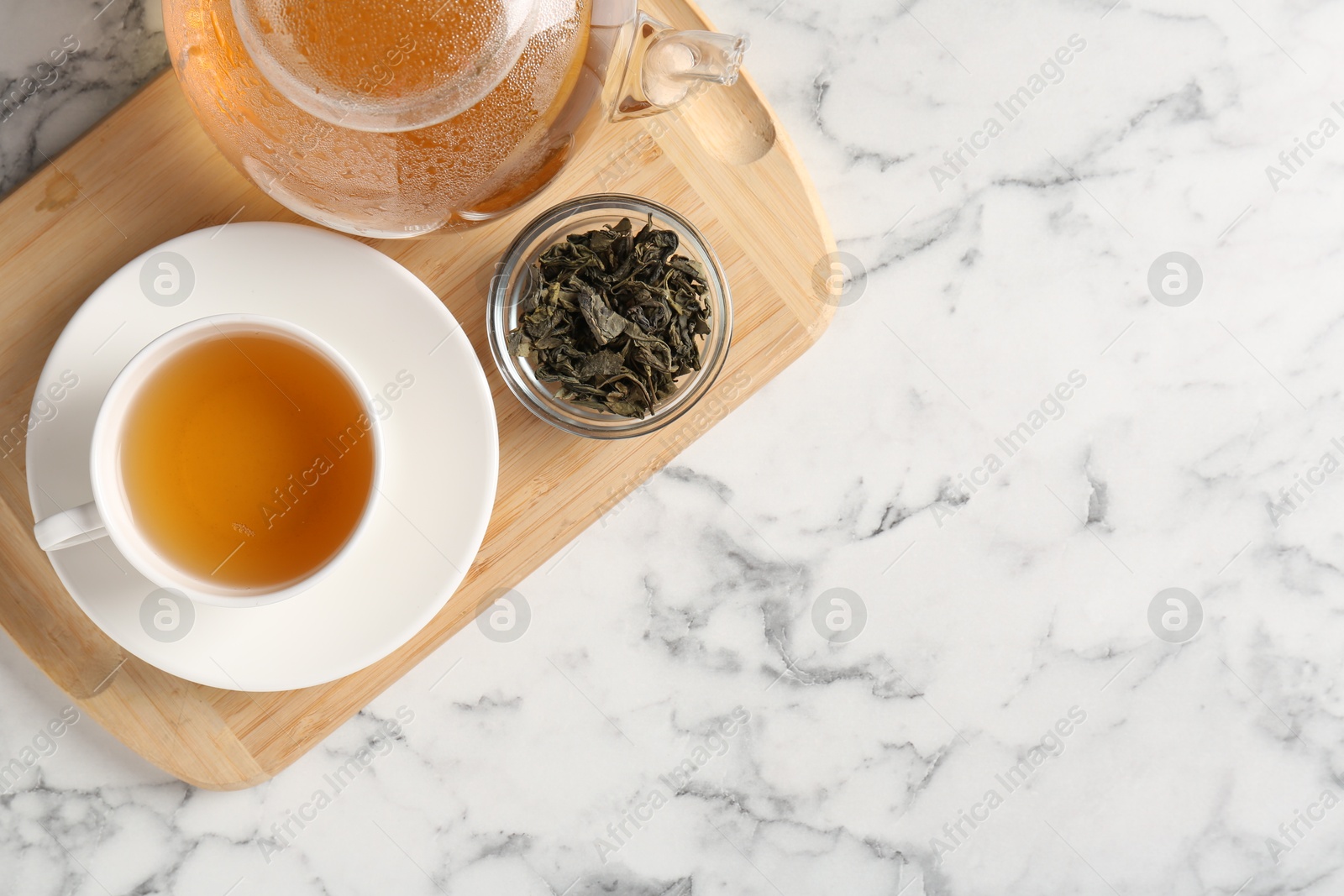 Photo of Refreshing green tea and dry leaves on white marble table, top view. Space for text