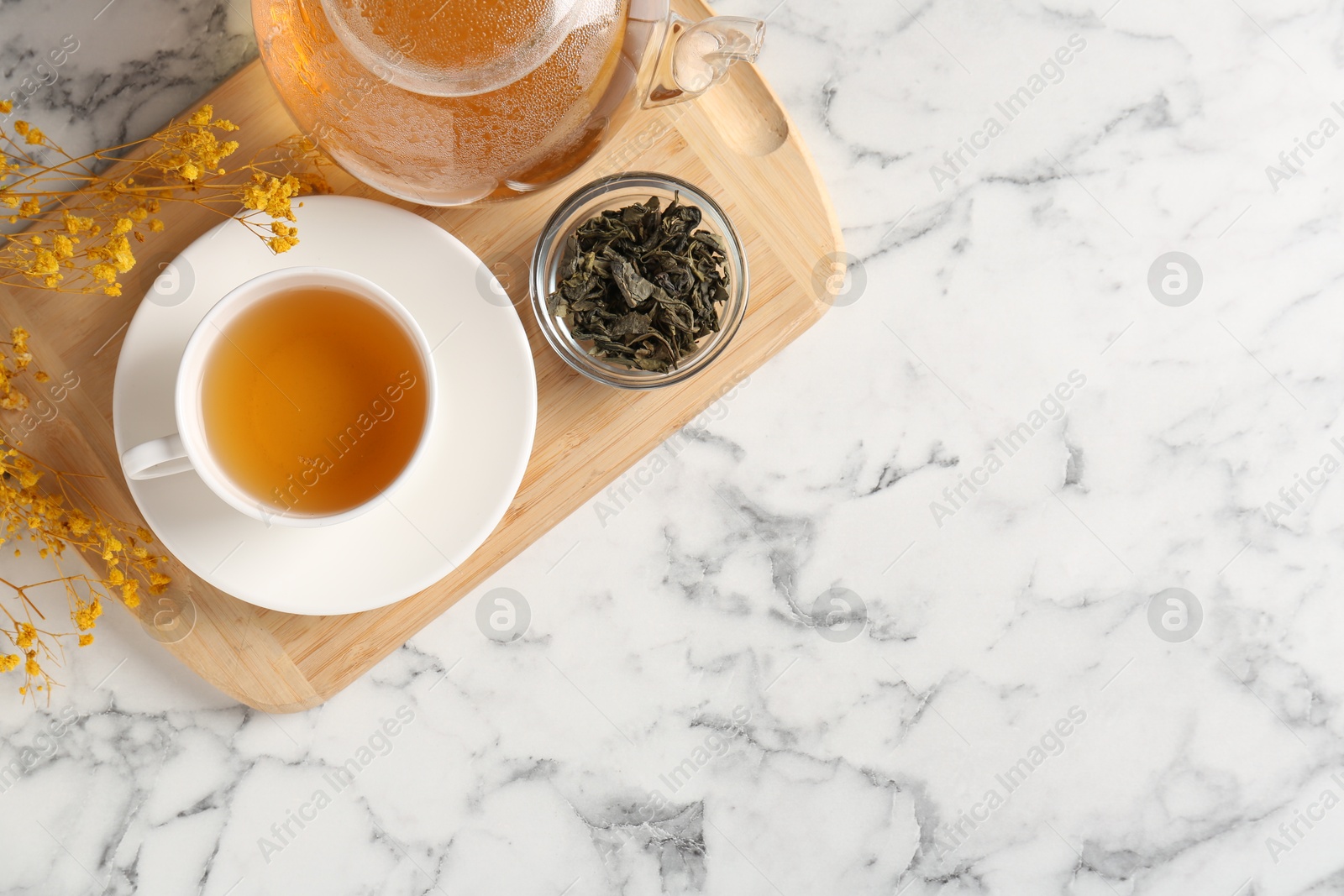 Photo of Refreshing green tea and dry leaves on white marble table, top view. Space for text