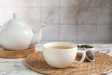 Photo of Refreshing green tea, strainer and dry leaves on white marble table, closeup