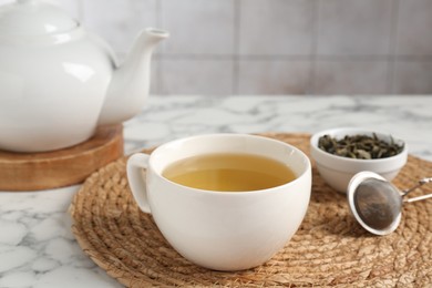 Photo of Refreshing green tea, strainer and dry leaves on white marble table, closeup