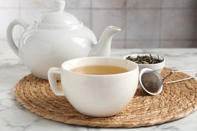 Photo of Refreshing green tea, strainer and dry leaves on white marble table, closeup