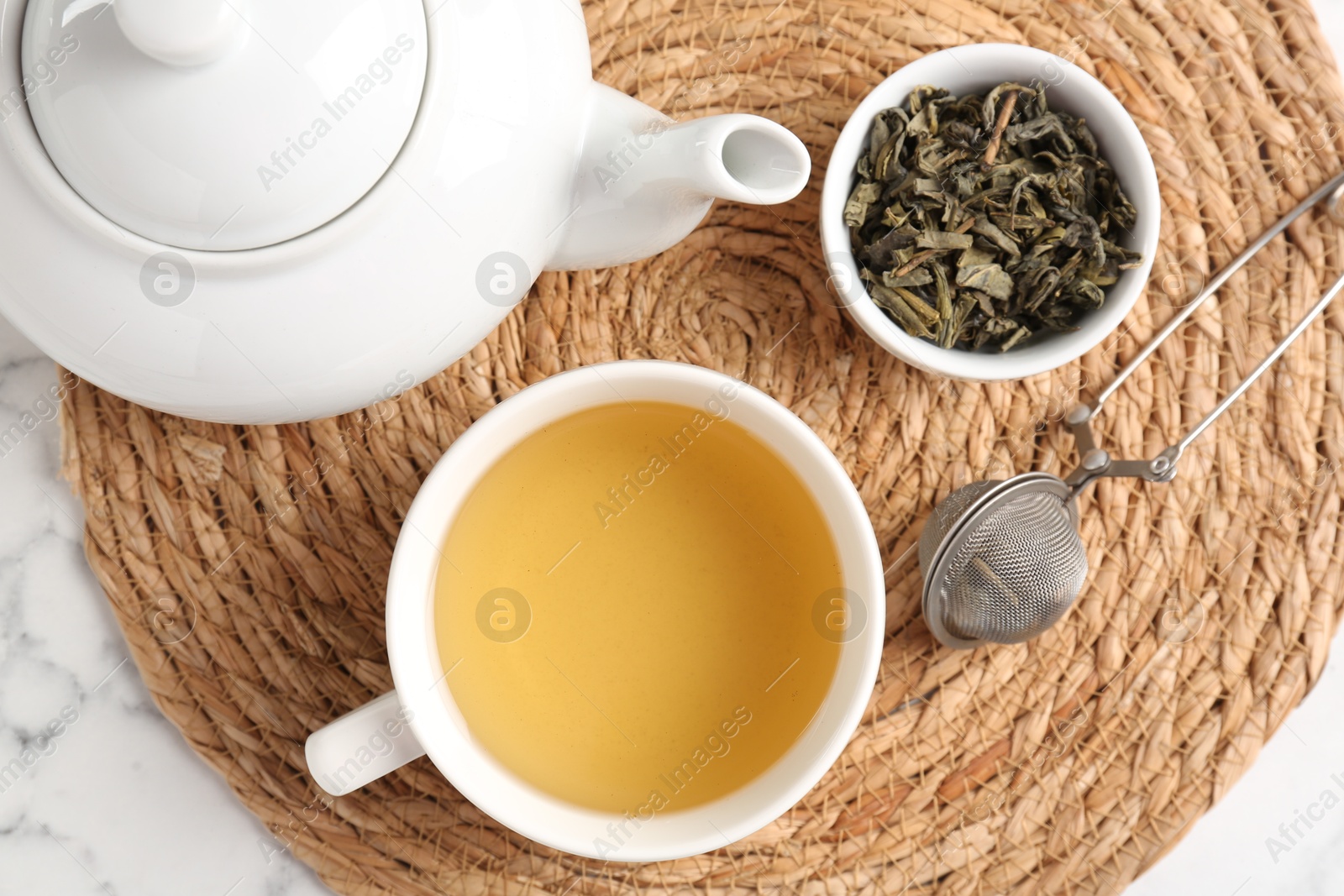 Photo of Refreshing green tea, strainer and dry leaves on white marble table, top view