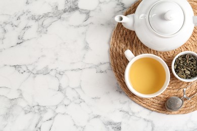 Photo of Refreshing green tea, strainer and dry leaves on white marble table, top view. Space for text