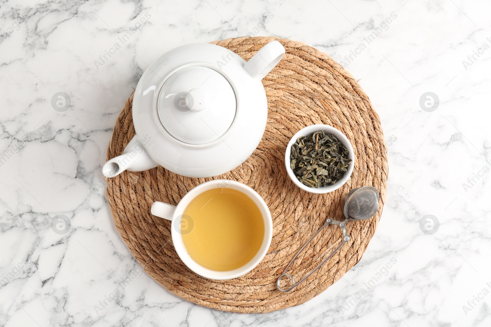 Photo of Refreshing green tea, strainer and dry leaves on white marble table, top view