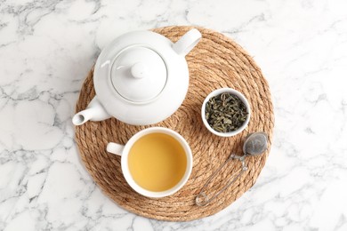 Photo of Refreshing green tea, strainer and dry leaves on white marble table, top view