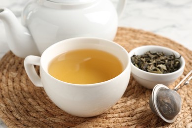 Photo of Refreshing green tea, strainer and dry leaves on white table, closeup