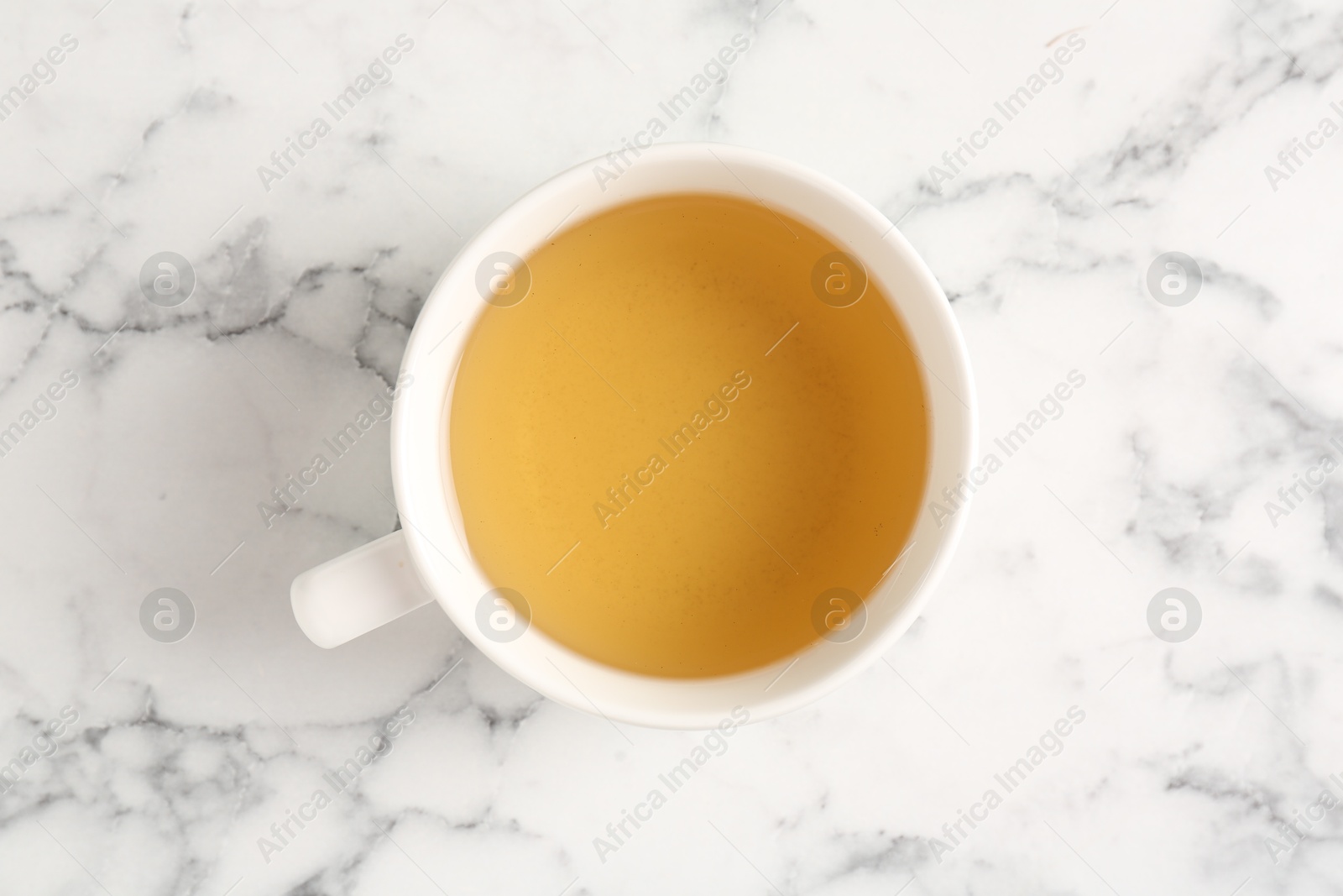 Photo of Refreshing green tea in cup on white marble table, top view