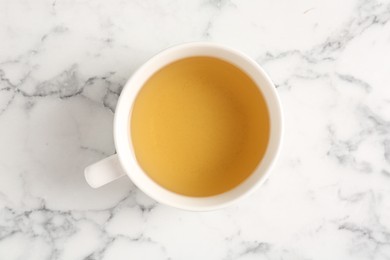 Photo of Refreshing green tea in cup on white marble table, top view