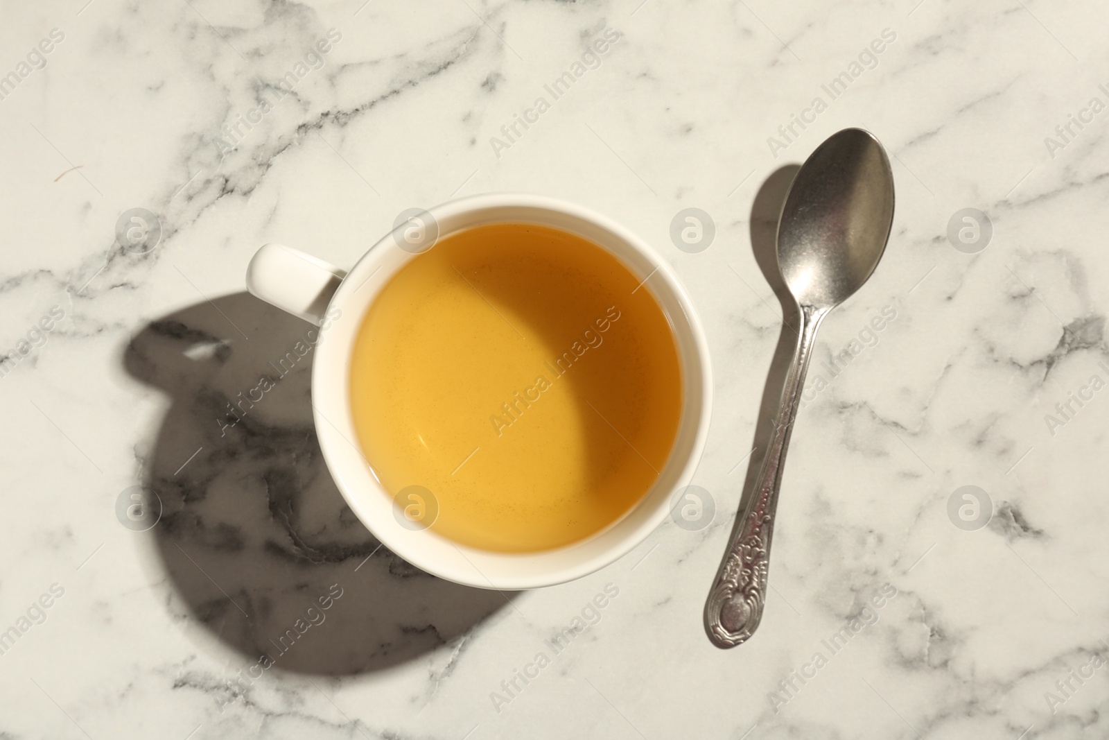 Photo of Refreshing green tea in cup and spoon on white marble table, top view