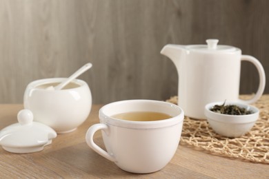 Photo of Refreshing green tea in cup, sugar bowl, dry leaves and teapot on wooden table, closeup