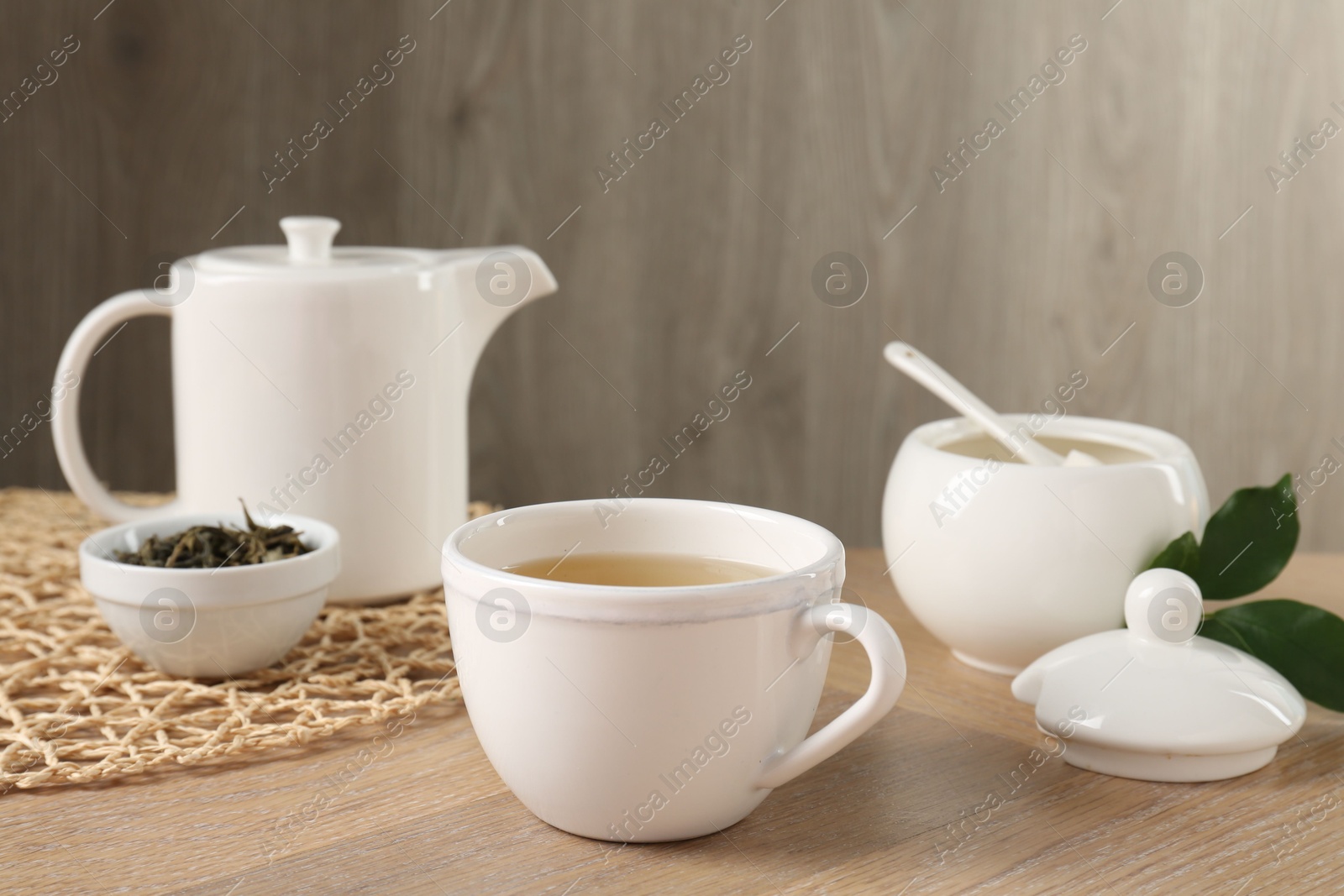 Photo of Refreshing green tea in cup, sugar bowl, leaves and teapot on wooden table