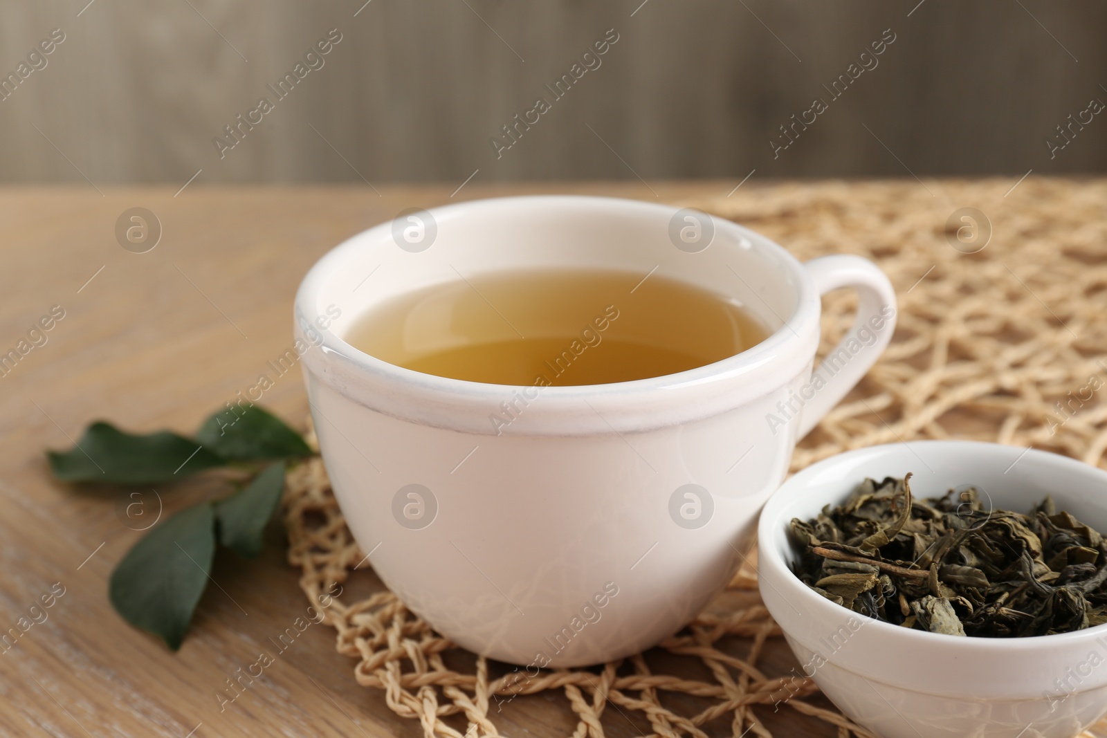 Photo of Refreshing green tea in cup and leaves on wooden table, closeup