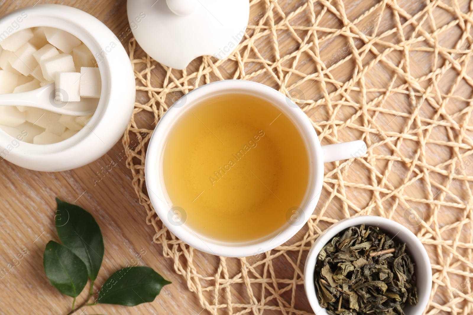 Photo of Refreshing green tea in cup, sugar bowl and leaves on wooden table, flat lay