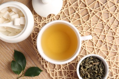 Photo of Refreshing green tea in cup, sugar bowl and leaves on wooden table, flat lay