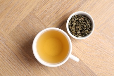 Photo of Refreshing green tea in cup and dry leaves on wooden table, top view