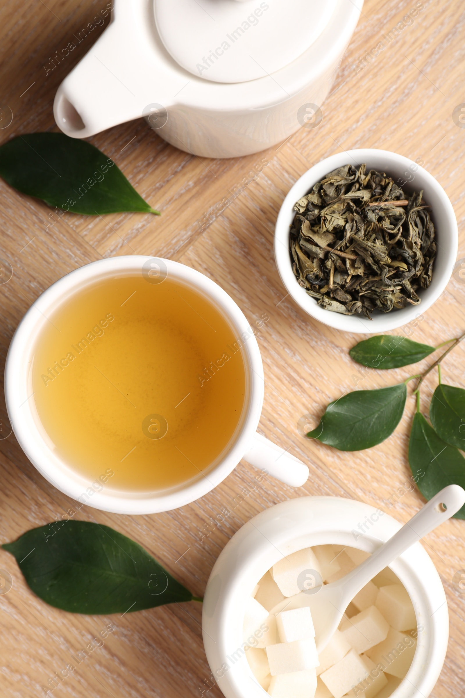 Photo of Refreshing green tea in cup, teapot, sugar bowl and leaves on wooden table, flat lay