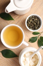 Photo of Refreshing green tea in cup, teapot, sugar bowl and leaves on wooden table, flat lay