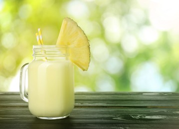 Image of Tasty pineapple cocktail or smoothie in mason jar on wooden table outdoors. Space for text