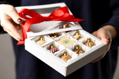 Photo of Woman holding box with tasty chocolate candies in shape of baubles on grey background, closeup