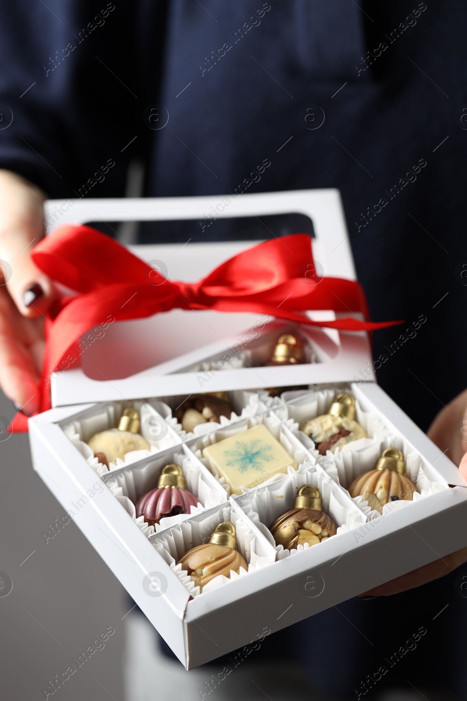 Photo of Woman holding box with tasty chocolate candies in shape of baubles on grey background, closeup