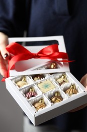 Photo of Woman holding box with tasty chocolate candies in shape of baubles on grey background, closeup