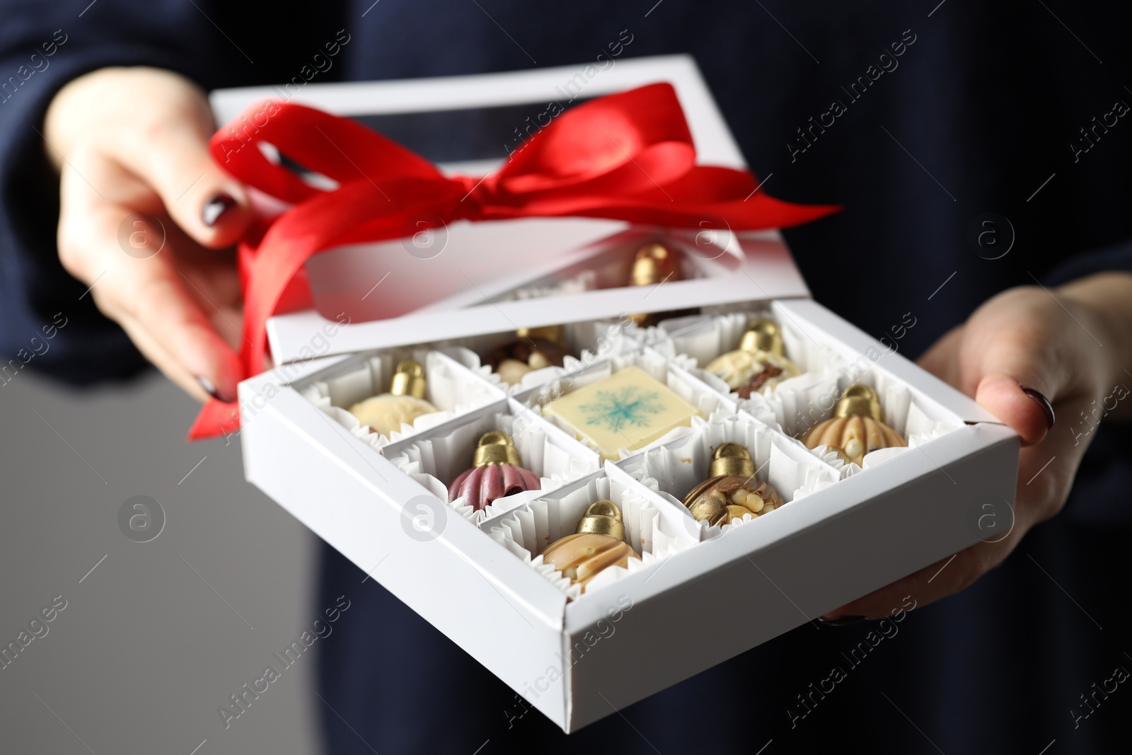 Photo of Woman holding box with tasty chocolate candies in shape of baubles on grey background, closeup