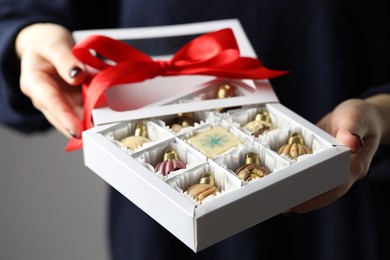 Photo of Woman holding box with tasty chocolate candies in shape of baubles on grey background, closeup