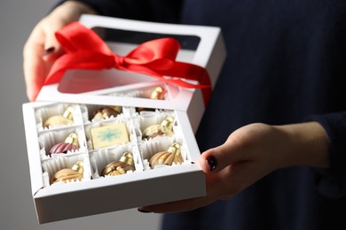 Photo of Woman holding box with tasty chocolate candies in shape of baubles on grey background, closeup