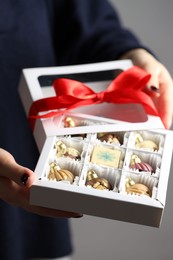 Photo of Woman holding box with tasty chocolate candies in shape of baubles on grey background, closeup