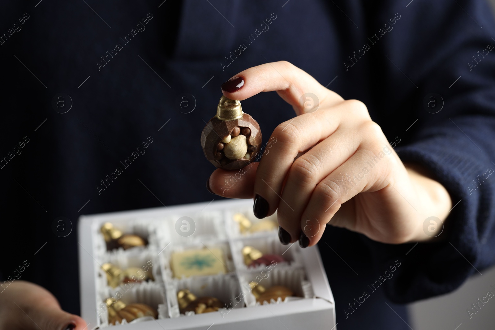 Photo of Woman holding box with tasty chocolate candies in shape of baubles on grey background, closeup