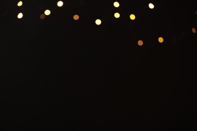 Photo of Blurred view of golden lights on black background, space for text. Bokeh effect