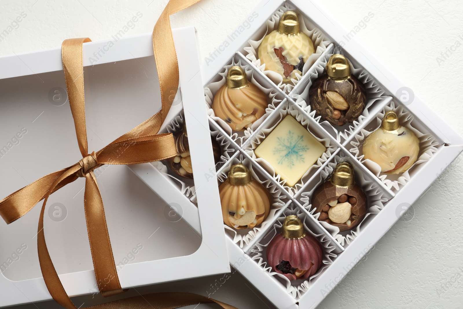 Photo of Box with tasty chocolate candies in shape of baubles on white background, top view