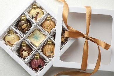 Photo of Box with tasty chocolate candies in shape of baubles on white background, top view