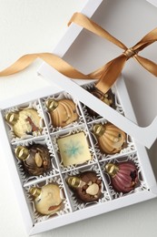 Photo of Box with tasty chocolate candies in shape of baubles on white background, top view