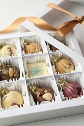 Photo of Box with tasty chocolate candies in shape of baubles on white background, closeup