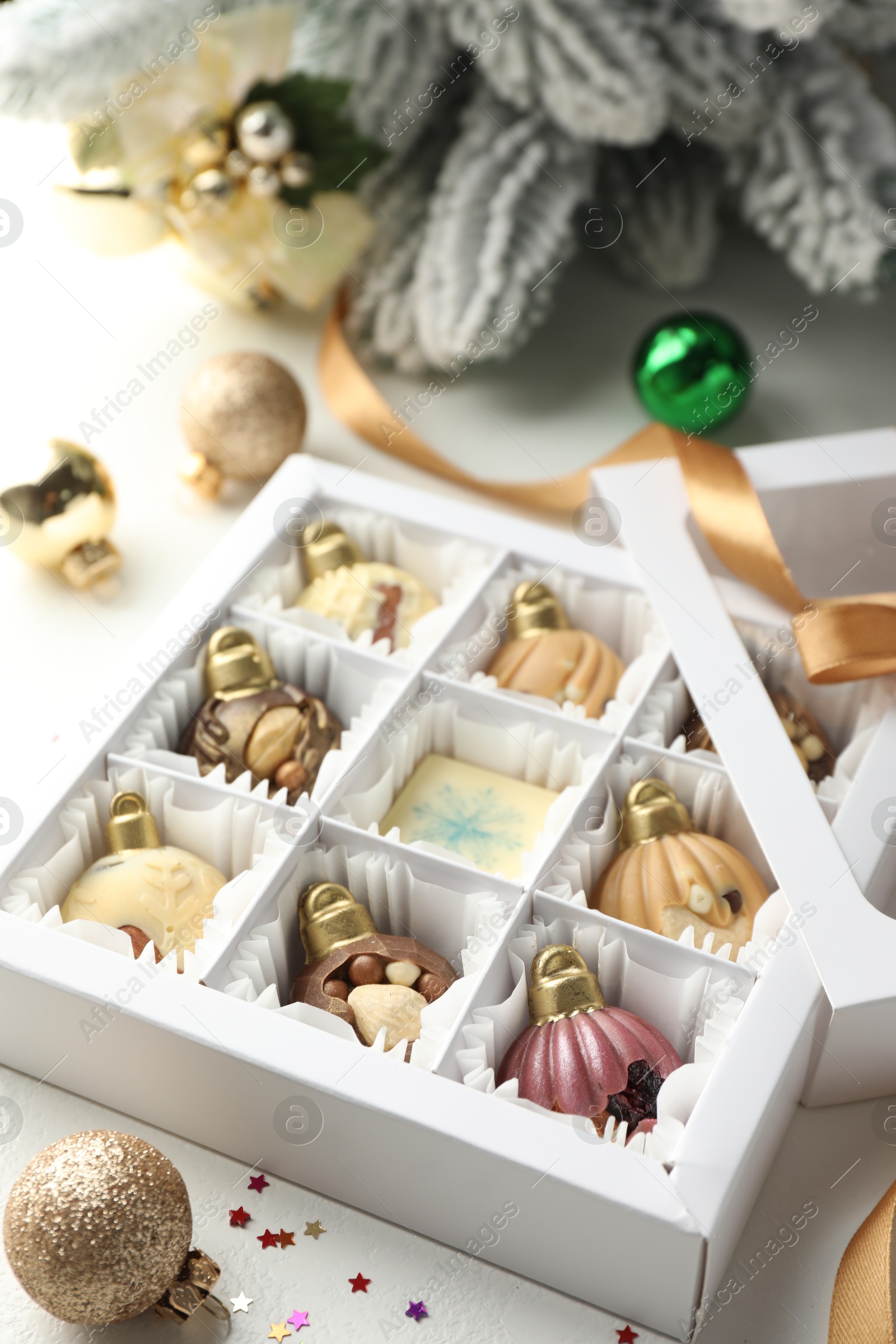 Photo of Box with tasty chocolate candies in shape of baubles and Christmas decor on white background, closeup