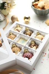 Photo of Box with tasty chocolate candies in shape of baubles and Christmas decor on white background, closeup