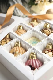 Photo of Box with tasty chocolate candies in shape of baubles and Christmas decor on white background, closeup