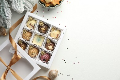 Box with tasty chocolate candies in shape of baubles and Christmas decor on white background, flat lay. Space for text