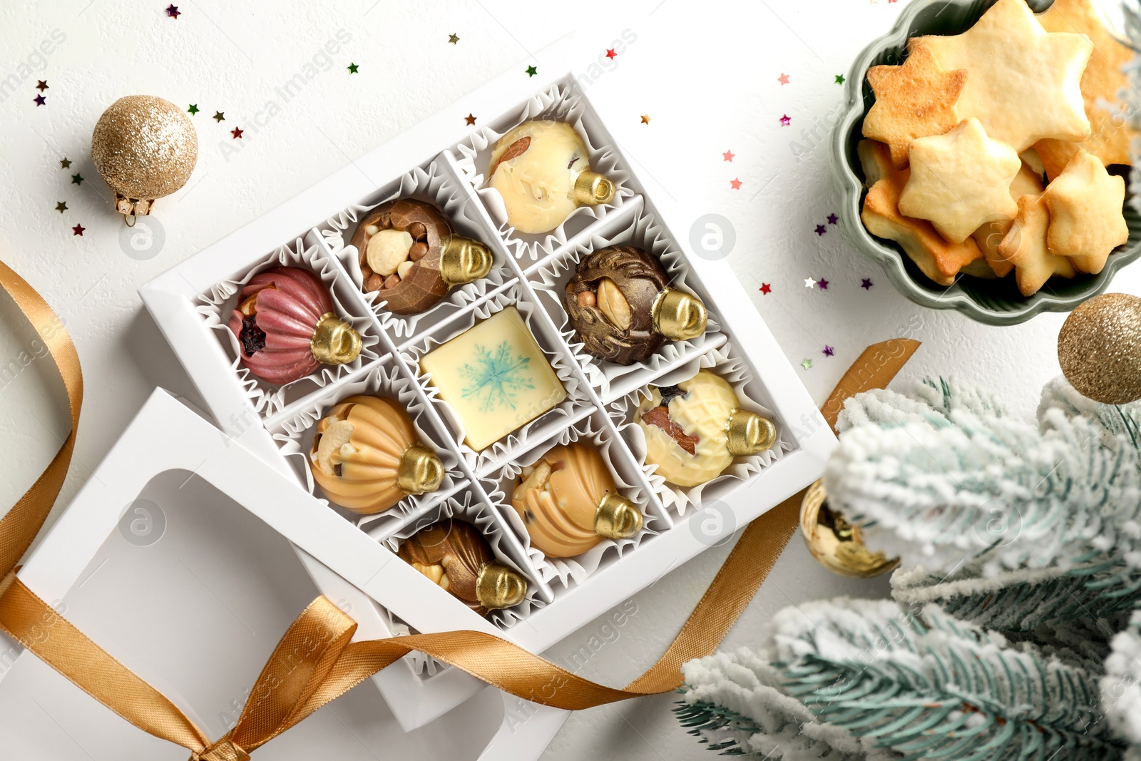 Photo of Box with tasty chocolate candies in shape of baubles and Christmas decor on white background, flat lay