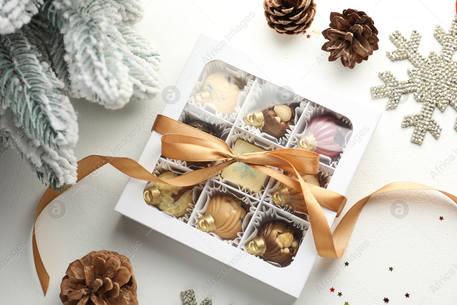 Photo of Box with tasty chocolate candies in shape of baubles and Christmas decor on white background, flat lay