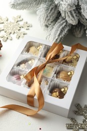 Photo of Box with tasty chocolate candies in shape of baubles and Christmas decor on white background, closeup