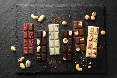 Photo of Different tasty chocolate bars with nuts and freeze dried raspberry on black table, flat lay