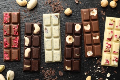 Photo of Different tasty chocolate bars with nuts and freeze dried raspberry on black table, flat lay